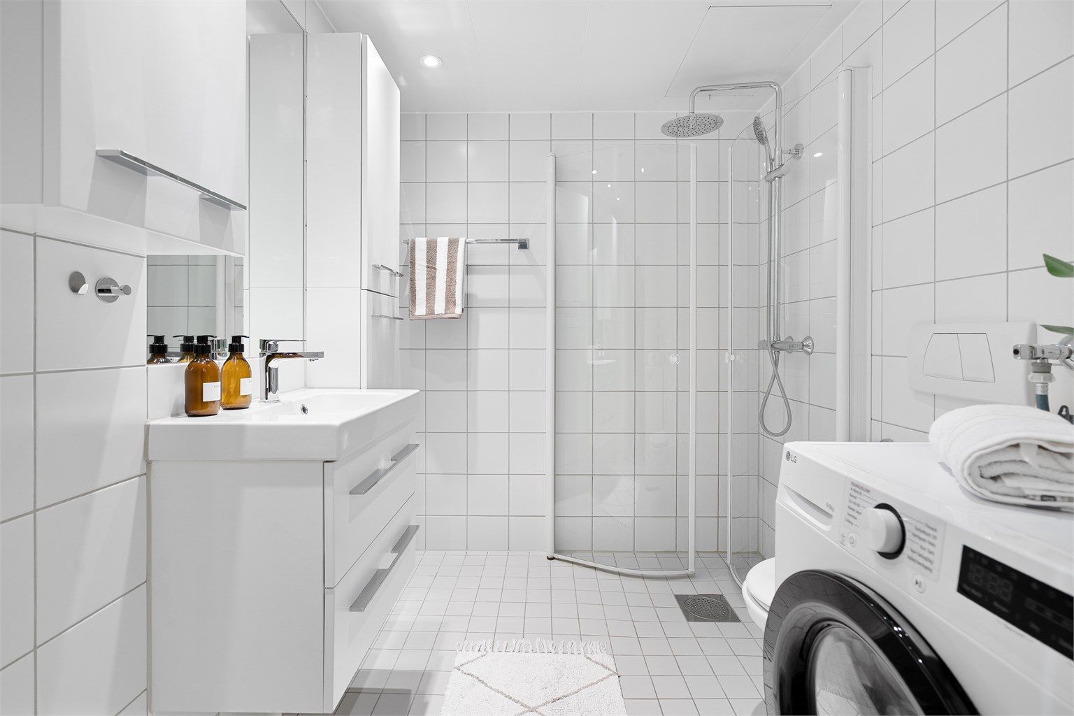Badet er praktisk innredet med vegghengt servantskap med skuffer, ovenpåliggende servant og speil med tilhørende veggskap og vegghengt toalett med innebygd sisterne.