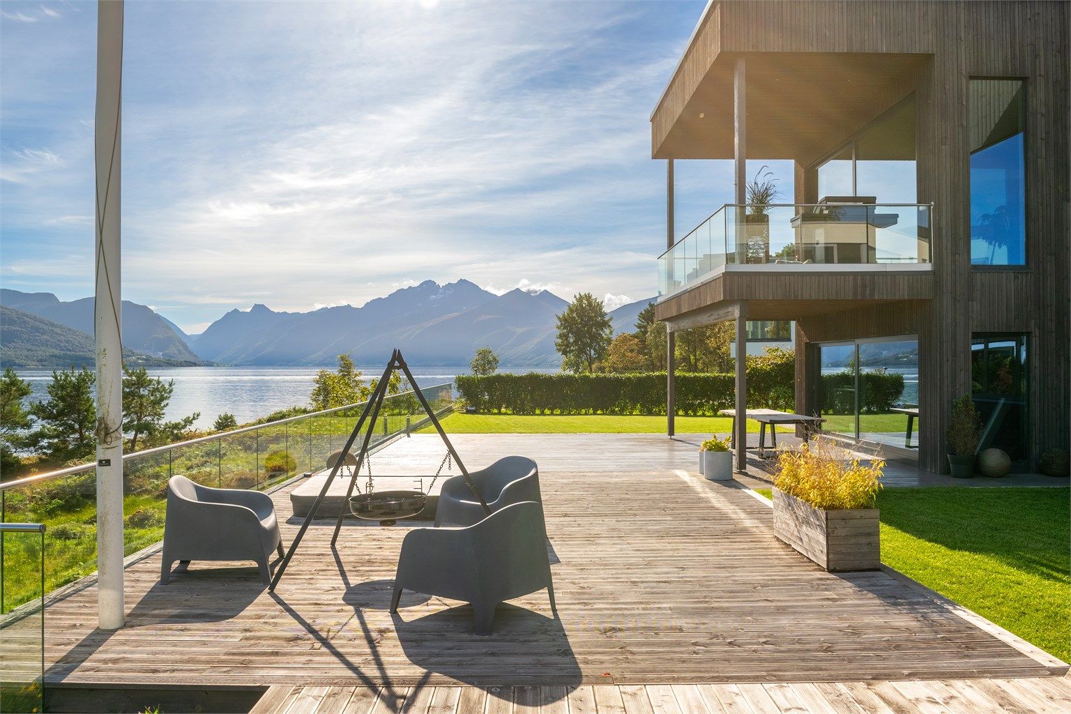 Sørøstvendt markterrasse med terrassebord og glassrekkverk mot sjøen.