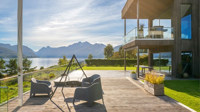Sørøstvendt markterrasse med terrassebord og glassrekkverk mot sjøen.