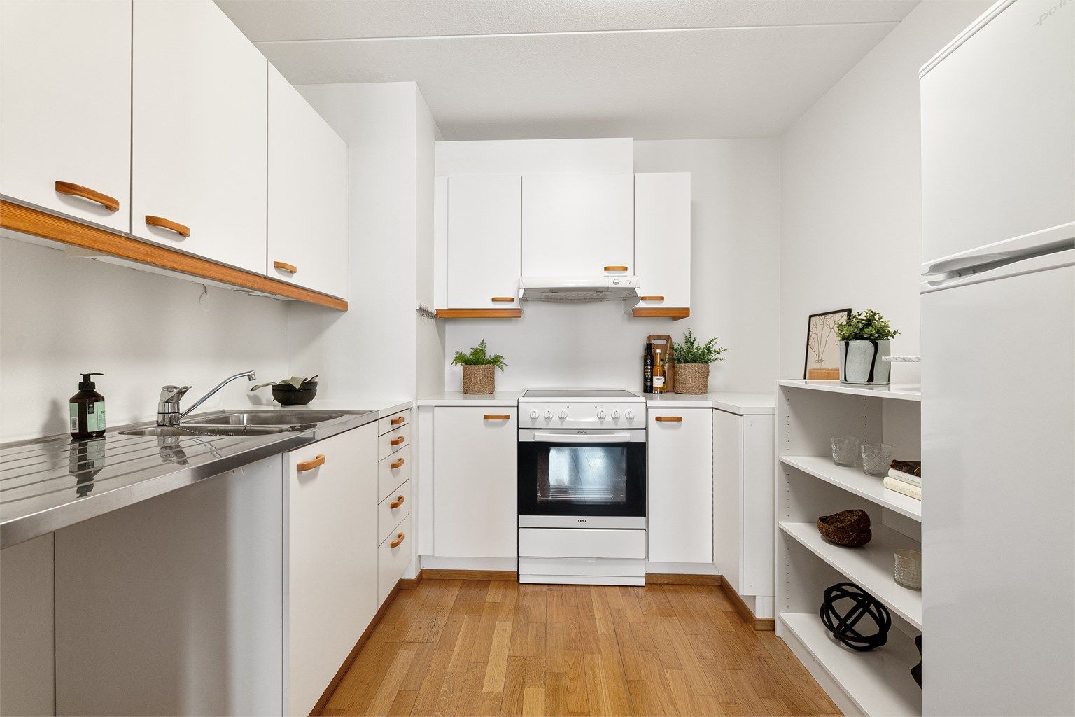 Kjøkkeninnredning med glatte, lyse fronter og benkeplater av laminat. Over komfyren er det ventilator med avtrekk, og husbrannslange er plassert under oppvaskkummen.