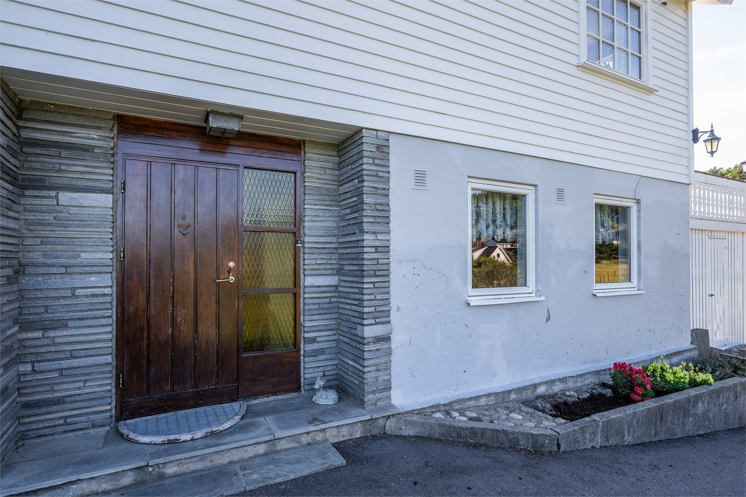 Inngangsparti med inntrukket ytterdør i teak og pusset murfasade. Velkommen inn!