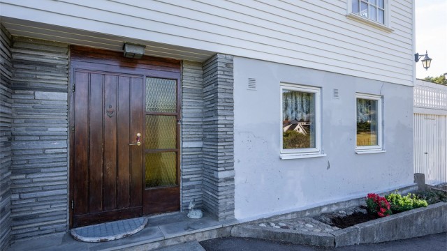 Inngangsparti med inntrukket ytterdør i teak og pusset murfasade. Velkommen inn!