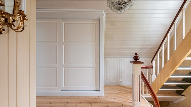 Gangens skyvdørsgarderobe er stedsbygget, med tilpassede dørblader i malt heltre.