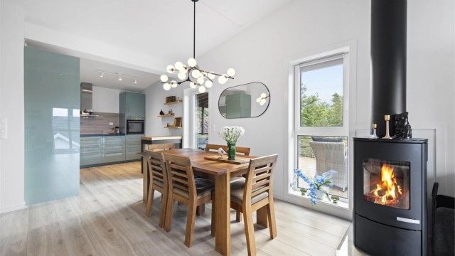 Spiseplass i åpen tilknytning til kjøkkenet, med peisovn og utsyn mot terrassen og naturen rundt.
