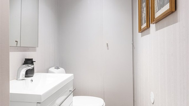 Toalettrom med gulvstående toalett og vegghengt servantinnredning.