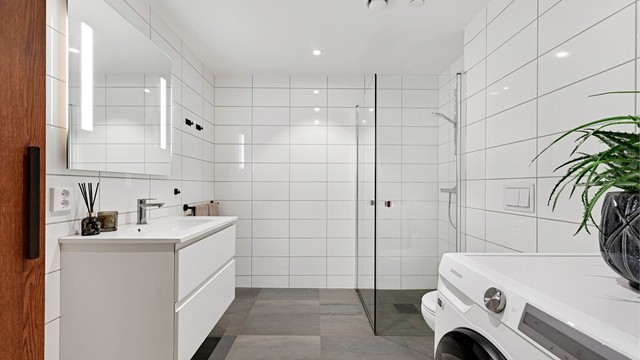 Badet har dusjhjørne med glassvegger, elektriske varmekabler og opplegg for vaskemaskin.