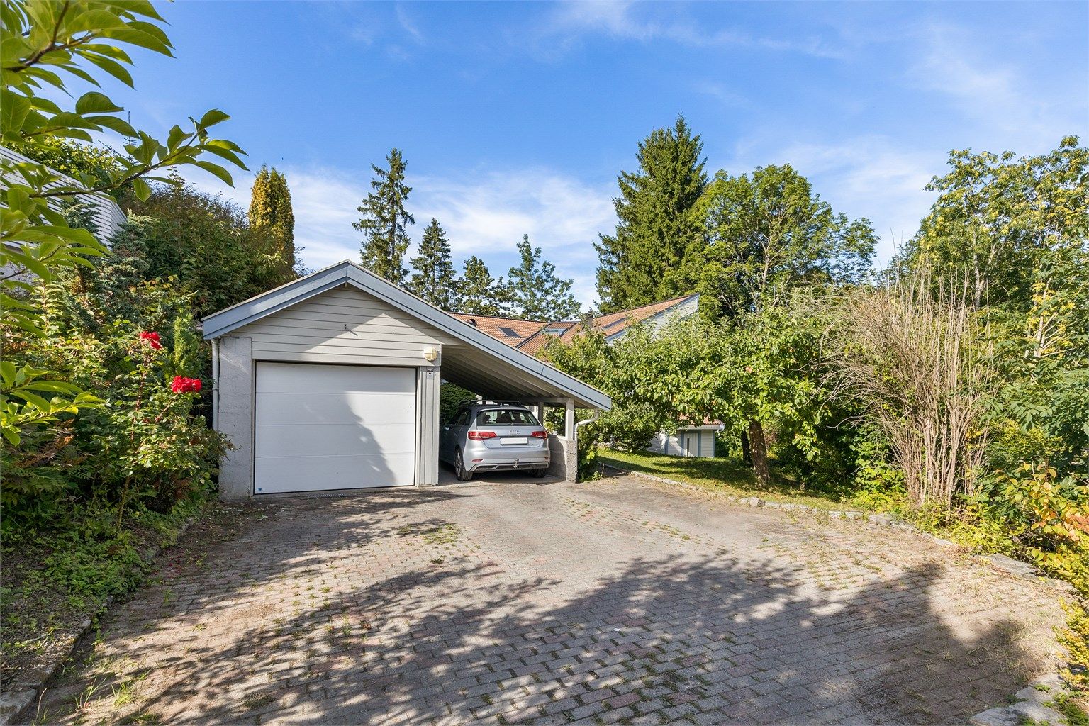 Frittstående garasje med carport og EL-billader. Gårdsplass med belegningsstein. 