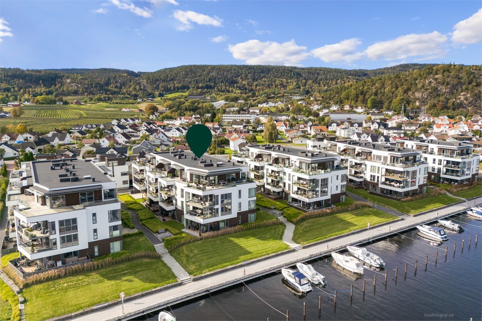 Foran bygningene er det etablert en sammenhengende fjordpromenade med småbåthavn og badeplass med sandstrand.