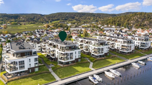 Foran bygningene er det etablert en sammenhengende fjordpromenade med småbåthavn og badeplass med sandstrand.