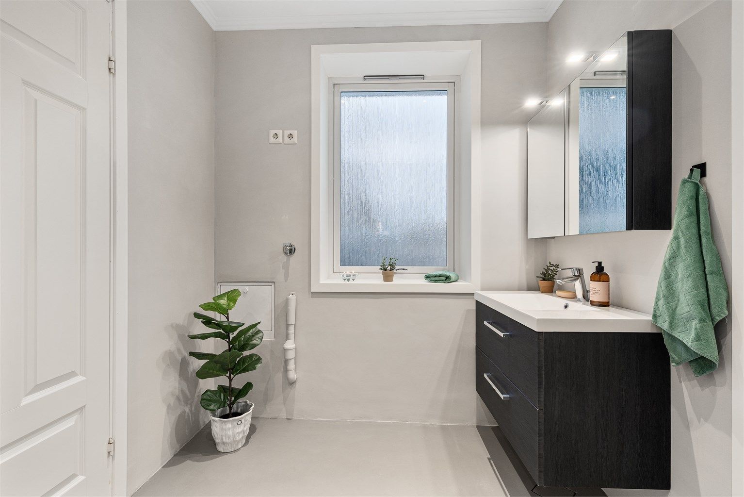 Den vegghengte innredningen har oppbevaring i skuffeseksjoner i tillegg til speilskapet med overlys. Baderommet har opplegg for vaskemaskin og tørketrommel og det er lagt varme i gulv