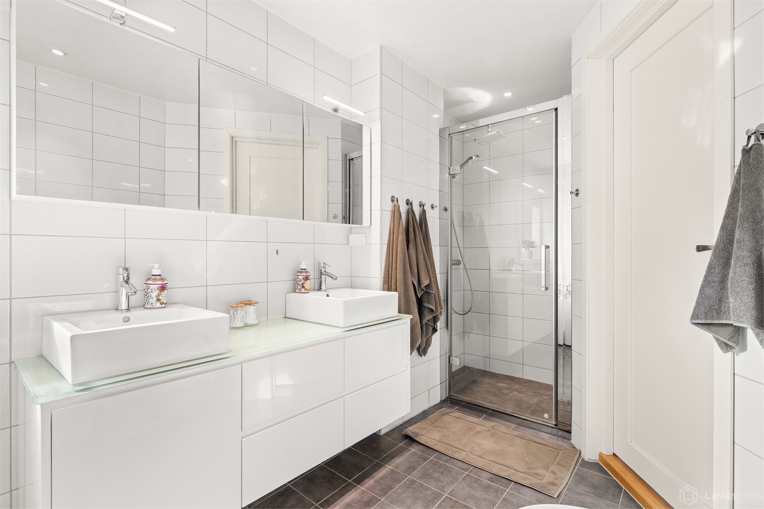 Innredningen har to ovenpåliggende servanter, speilskap og en separat dusjnisje med glassdør.