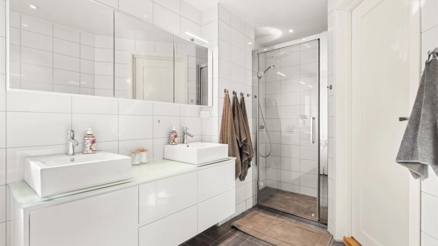 Innredningen har to ovenpåliggende servanter, speilskap og en separat dusjnisje med glassdør.