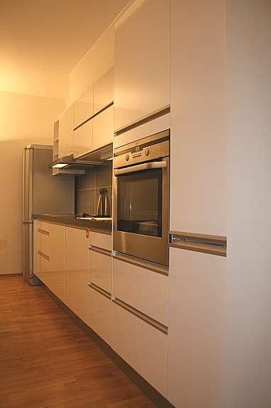 Eldre bilde av kjøkken med komfyr, platetopp, ny oppvaskmaskin og kombiskap kjøl/frys. 