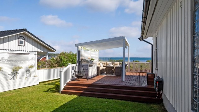 På nordvestsiden av verandaen er det bygd en pergola med tett, transparent tak, stort vindu mot utsikten, varmelamper og et plassbygd utekjøkken med grill i ytterste del.