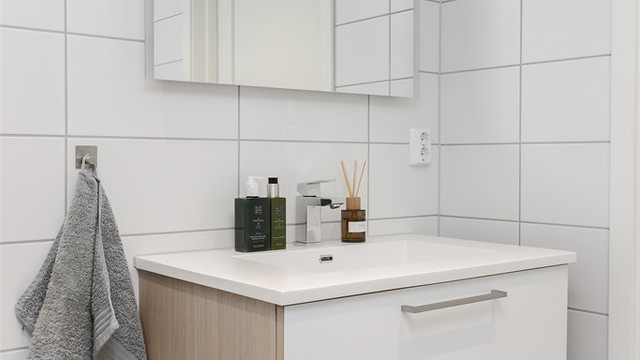 Badet har vegghengt toalett, servantinnredning og et dusjhjørne med regnfalls- og hånddusj.