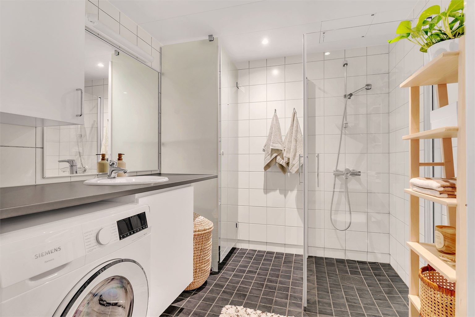 Innbydende og meget romslig bad med hvite fliser på vegg, gråmelerte fliser med varme i gulv og downlights i himling.