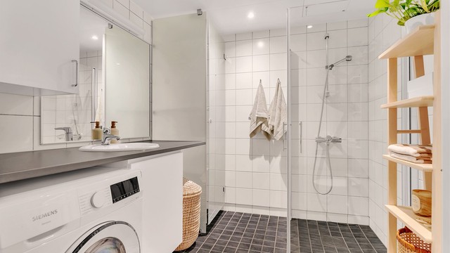 Innbydende og meget romslig bad med hvite fliser på vegg, gråmelerte fliser med varme i gulv og downlights i himling.