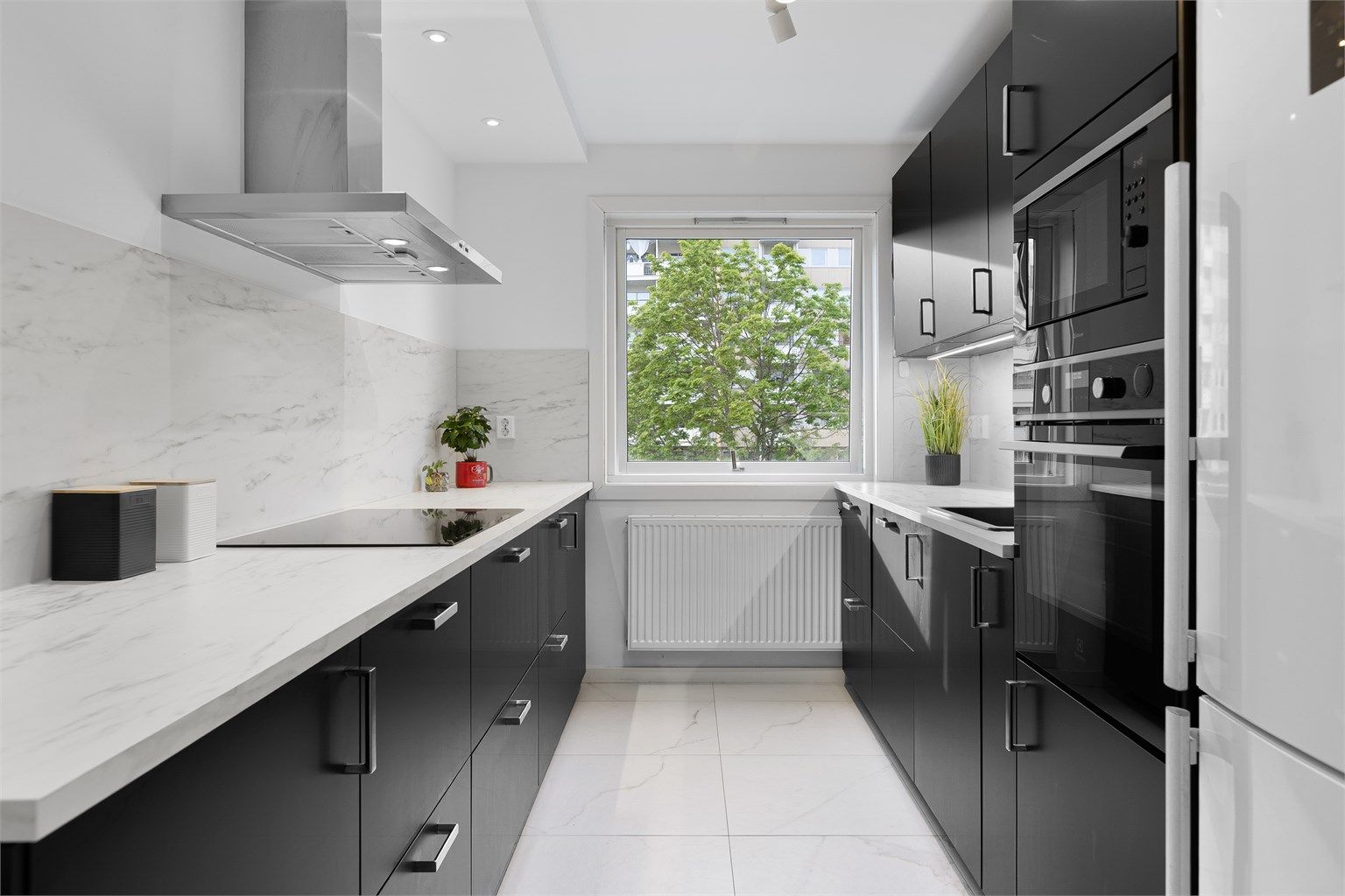 Moderne kjøkken med slette fronter. Vegghengt ventilator og integrerte hvitevarer. Frittstående kjøleskap og plass til fryseboks.