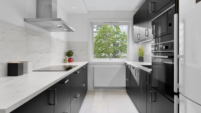 Moderne kjøkken med slette fronter. Vegghengt ventilator og integrerte hvitevarer. Frittstående kjøleskap og plass til fryseboks.