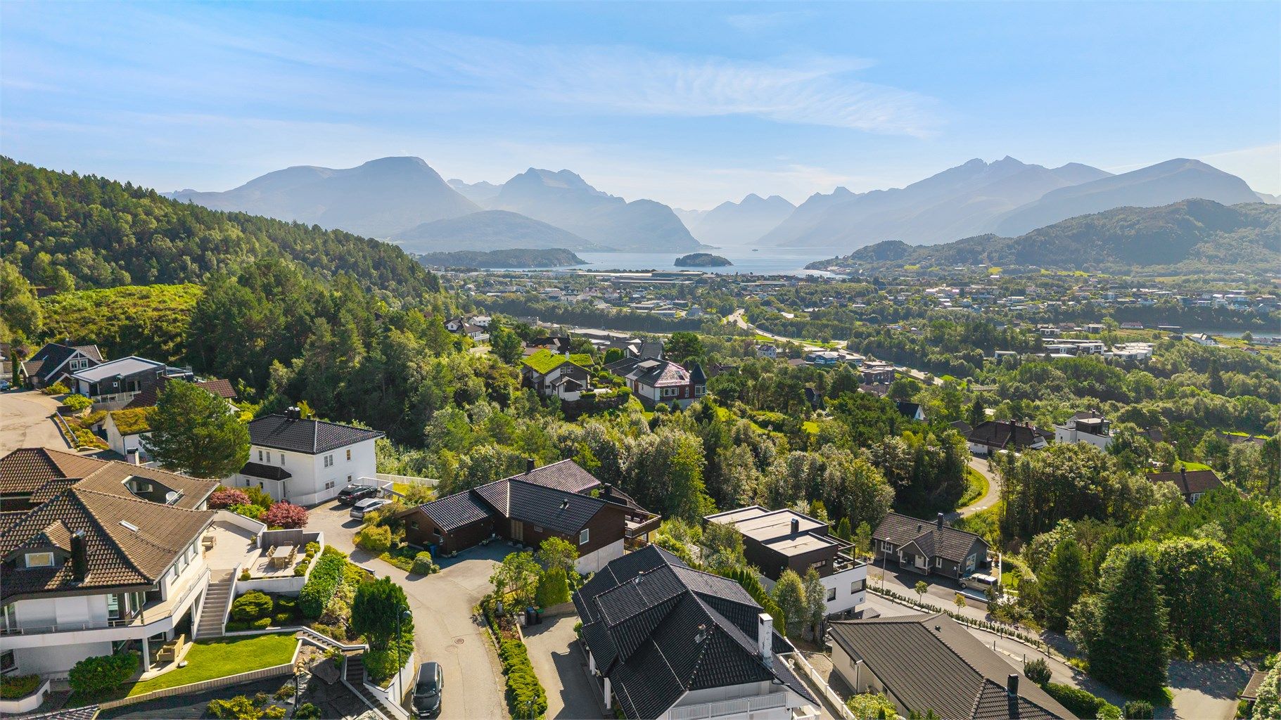 Dronebilde av boligen og nærområdet mot Storfjorden og innløpet til Hjørungfjorden, omkranset av Sunnmørsalpane