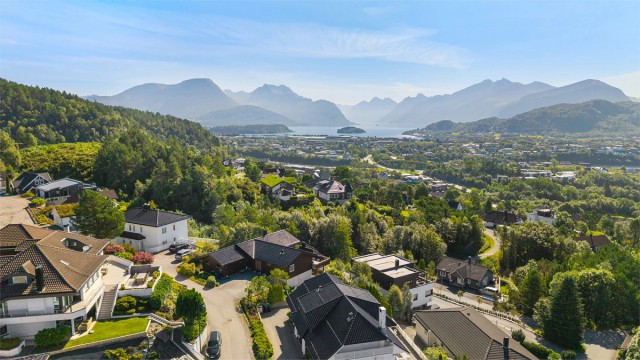 Dronebilde av boligen og nærområdet mot Storfjorden og innløpet til Hjørungfjorden, omkranset av Sunnmørsalpane