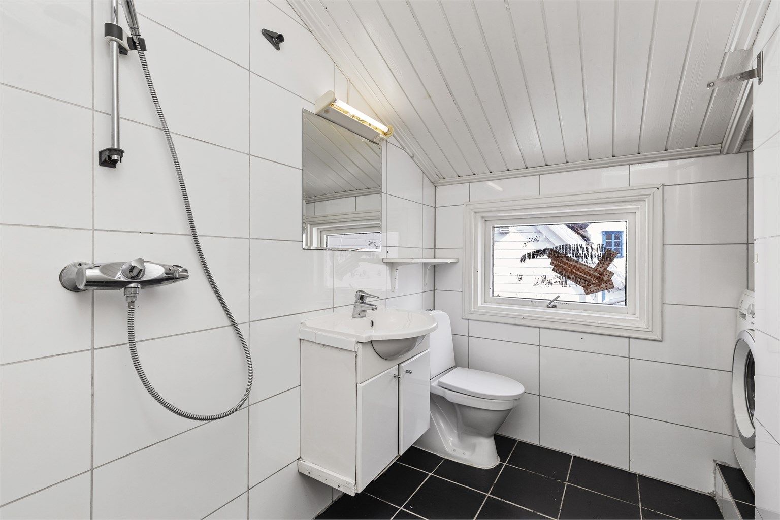 Badet har flislagt gulv, panel i taket og dusjløsning.