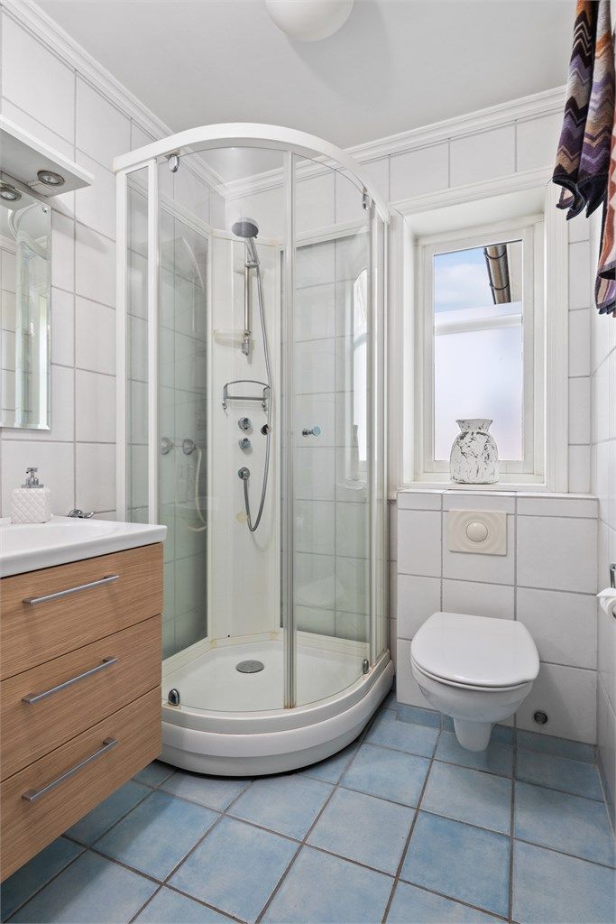 Badet nede er innredet med hvite veggfliser og lyseblå fliser på gulvet.