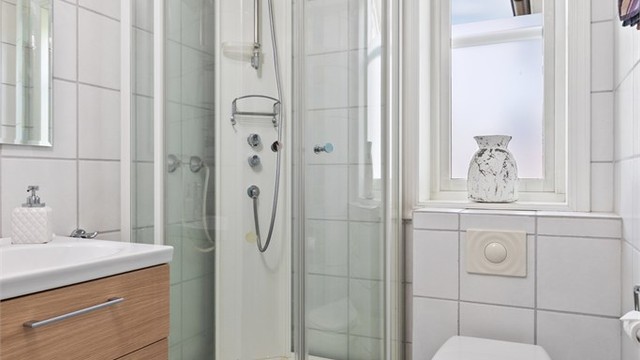 Badet nede er innredet med hvite veggfliser og lyseblå fliser på gulvet.
