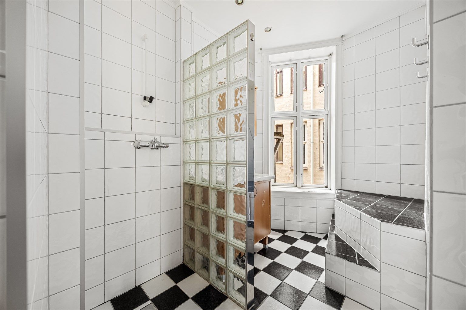 Lyst bad med dusj på gulv med halvvegg i glassbyggerstein.