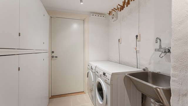 Praktisk bod i kjeller med flislagt gulv, gulvvarme og opplegg for vaskemaskin.