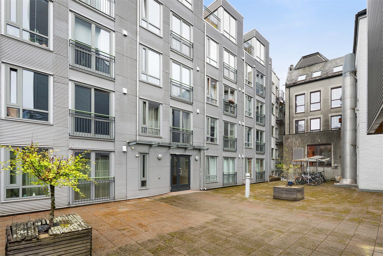Felles atrium med sittebenker og beplantning. Uteområde med sykkelparkering og inngang til borettslagets oppganger.