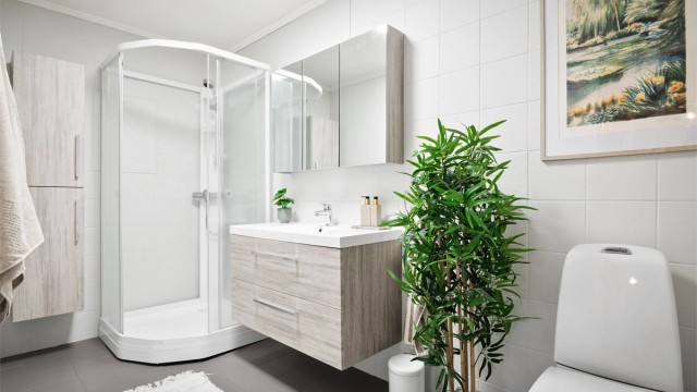 Flislagt baderom med gulvvarme. Badet er innredet med vegghengt servantinnredning med ovenpåliggende servant, speilskap med stikkontakt på vegg over servant og dusjkabinett.