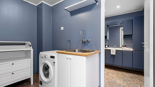 Praktisk vaskeromsdel med opplegg for vaskemaskin og vegghengt utslagsvask. Fra vaskerommet er det dør videre inn til badet.
