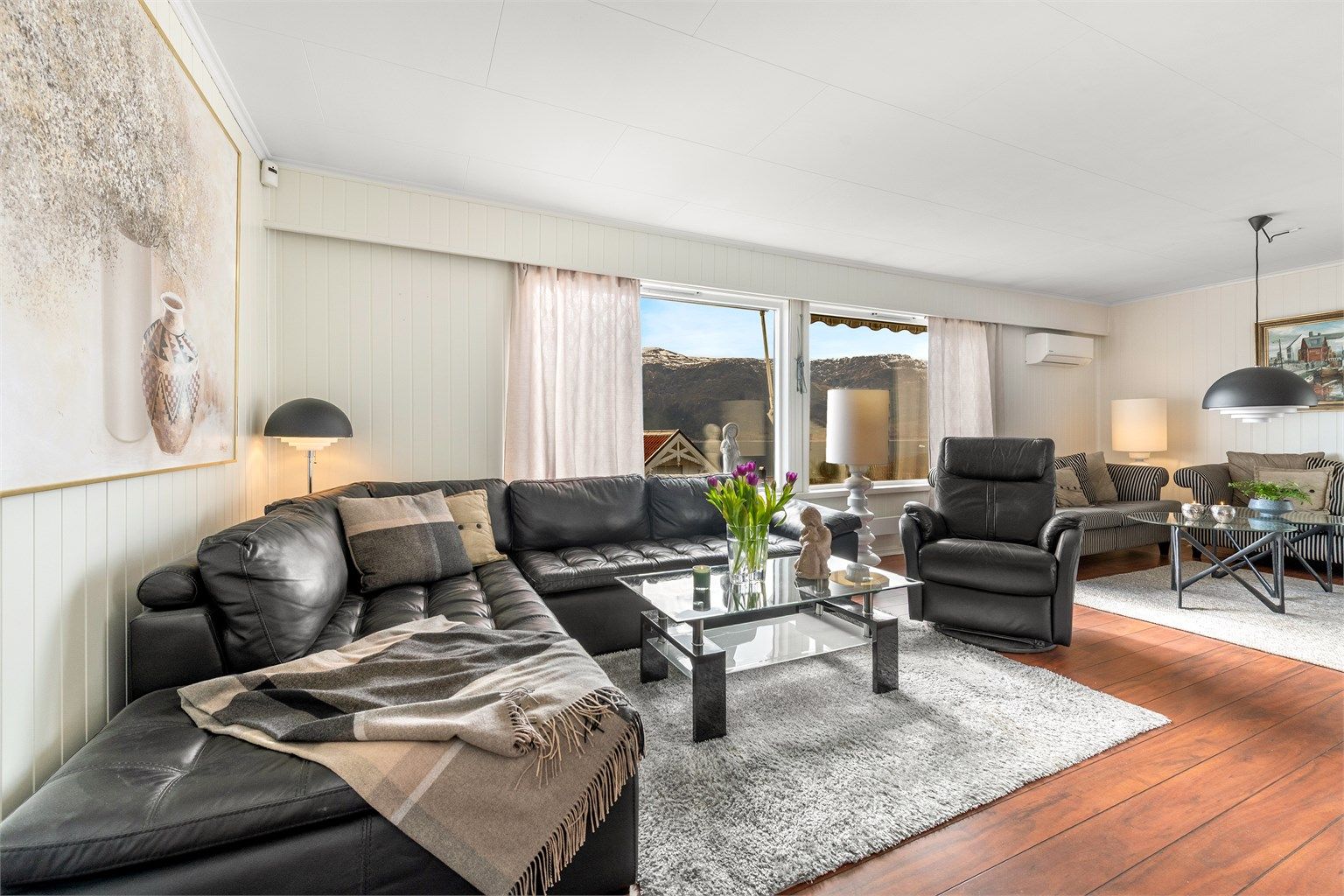 Stuen har store vindusflater som rammer inn utsikten. For komfort og effektiv oppvarming er det installert en luft-til-luft varmepumpe i 2022.