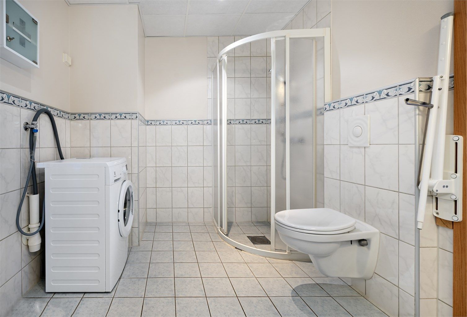 Badet er utstyrt med veggmontert toalett, dusjhjørne og opplegg for vaskemaskin.