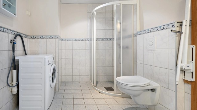 Badet er utstyrt med veggmontert toalett, dusjhjørne og opplegg for vaskemaskin.