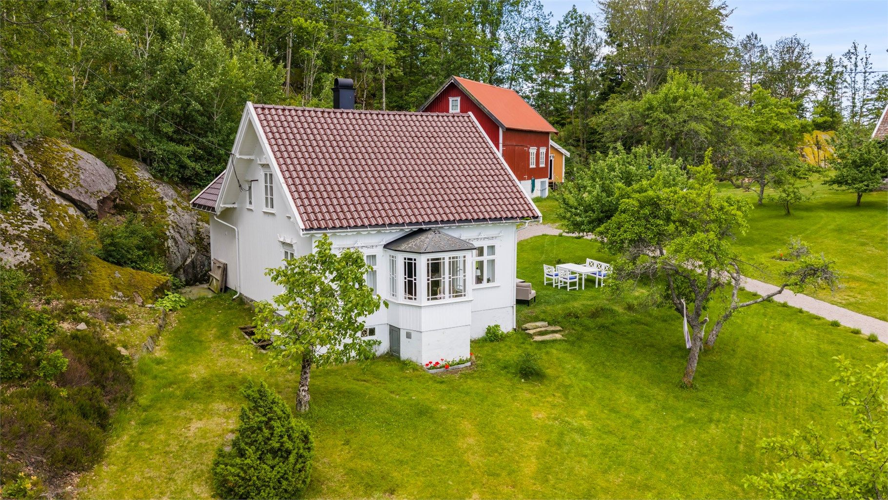 Hovedhuset med sin karakteristiske karnapp ligger skjermet og solrikt til, omgitt av idyllisk hage.
