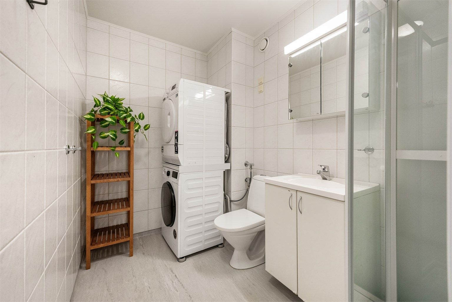 Badet har flislagte vegger, dusjkabinett og servantinnredning.