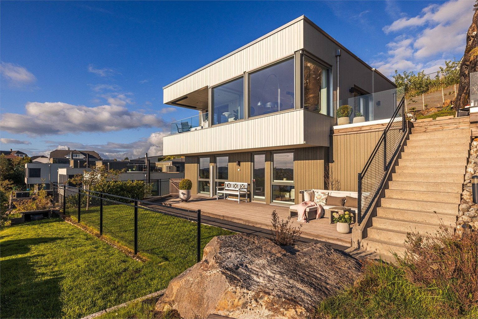 Eneboligen har en moderne arkitektur med store vinduer og rette linjer. Kledd med trekledning, rekkverk i glass og støpt trapp med belysning.