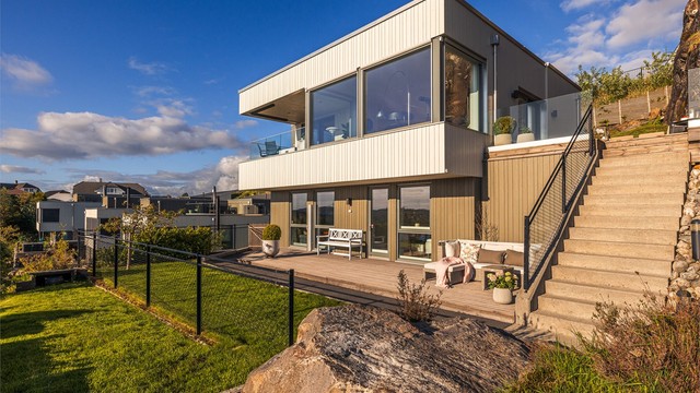 Eneboligen har en moderne arkitektur med store vinduer og rette linjer. Kledd med trekledning, rekkverk i glass og støpt trapp med belysning.