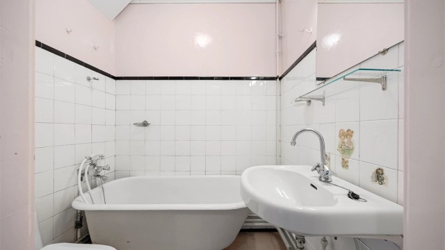 Baderom fra byggeår, utstyrt med frittstående badekar, toalett og servant med speil og belysning.