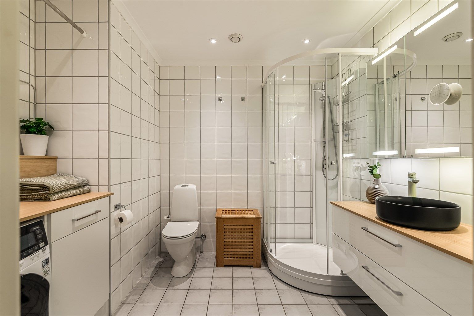 Dusjkabinett med glassvegger, gulvstående toalett og innfelte downlights i himling.