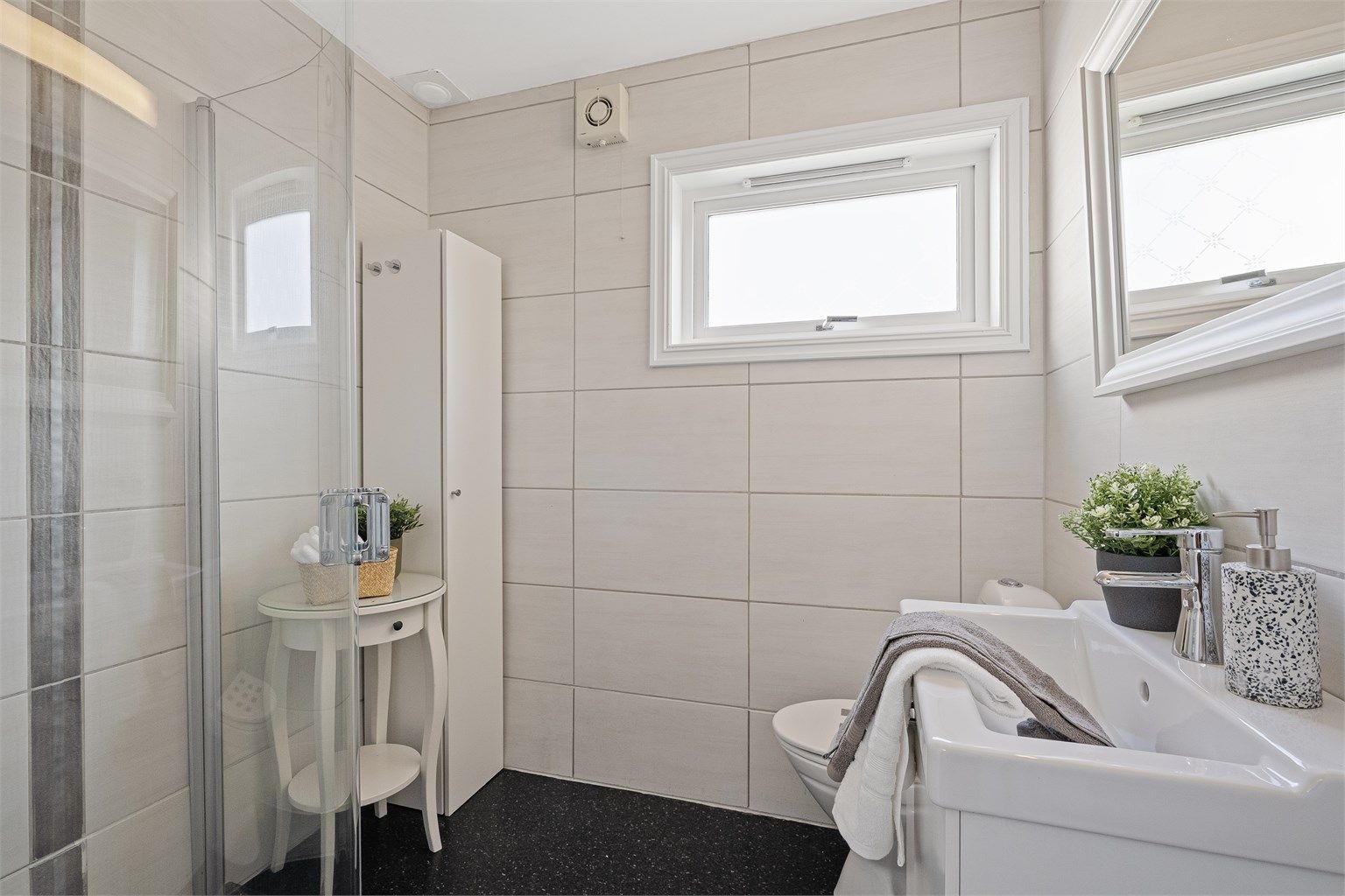 Fint bad som var nytt i 2005. Badet ble pusset opp av fagfolk og er tidløst med lyse fliser på vegg og belegg på gulv.  Vegghengt toalett, dusjhjørne med innfellbare dører og servant med skuffer. Speil på vegg.  