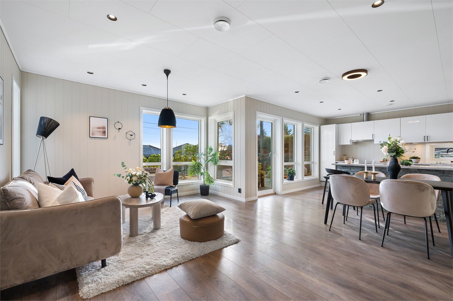 Lys og moderne stue med åpen løsning mot kjøkken og spiseplass og store vindusflater som gir flott romfølelse og godt lysinnslipp