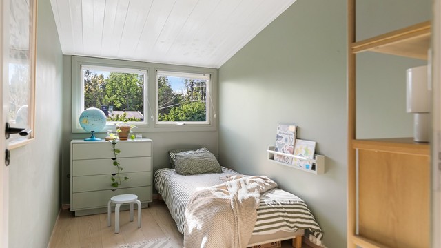 Soverom med parkett på gulv, panel i himling og plass til seng og oppbevaring.