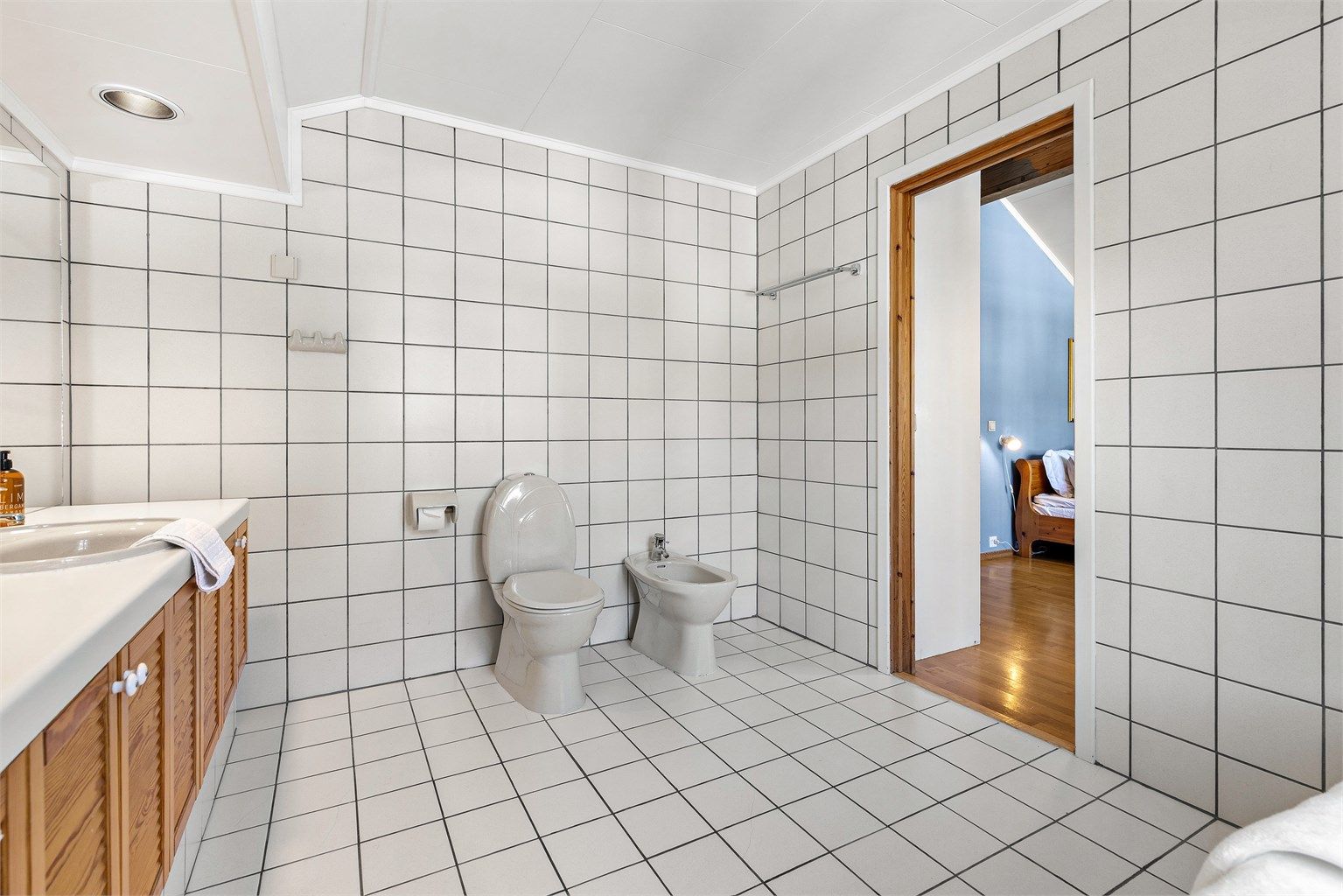 Baderom tilhørende soverom 1 er av god størrelse, og har gulvstående servantinnredning med dobbel ovenpåliggende servant med armaturer. Det er også stort speil med overlys, badekar med vegghengt armatur og gulvstående toalett og bidé. 
