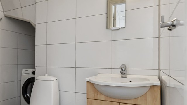 Badet har fliser på gulv og vegger, og er utstyrt med dusjhjørne og opplegg for vaskemaskin.
