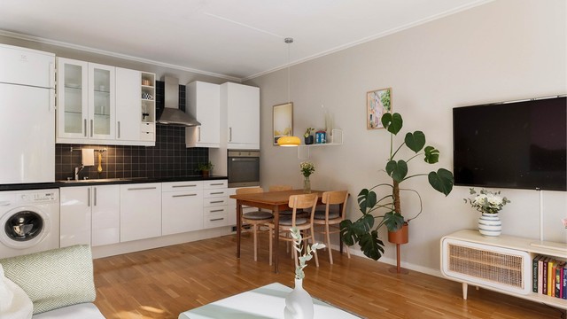 Her kan du plassere spisebord, sofagruppe og TV-møbel slik det passer deg best. Kjøkkenet med hvite, glatte fronter og mørke fliser glir naturlig inn i helheten og gir et rent og tidløst uttrykk.
