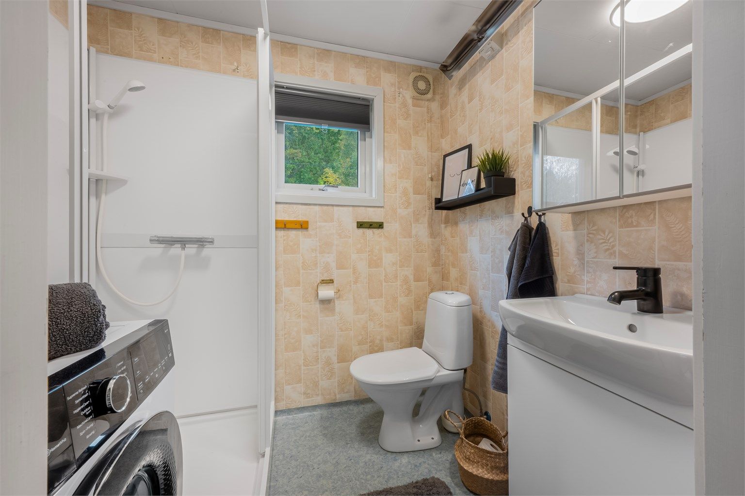 Badet i 1. etasje er innredet med dusjkabinett, toalett, servantmøbel og opplegg for vaskemaskin.