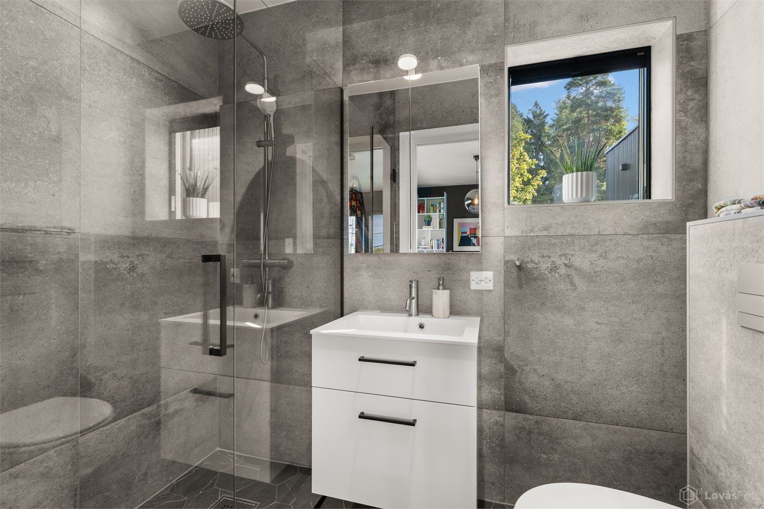 Master-badet holder en moderne og smakfull standard med store flislagte overflater, gulvvarme og downlights i tak. Badet er innredet med vegghengt servantinnredning, speil med belysning, vegghengt toalett og en romslig dusjsone.